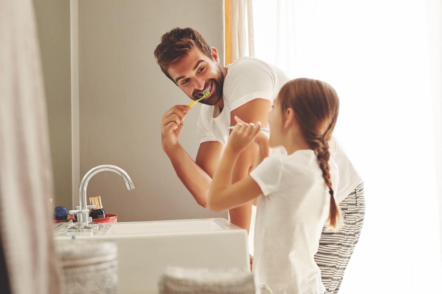 Father and dughter practice good oral health at home by brushing their teeth in Cornelius